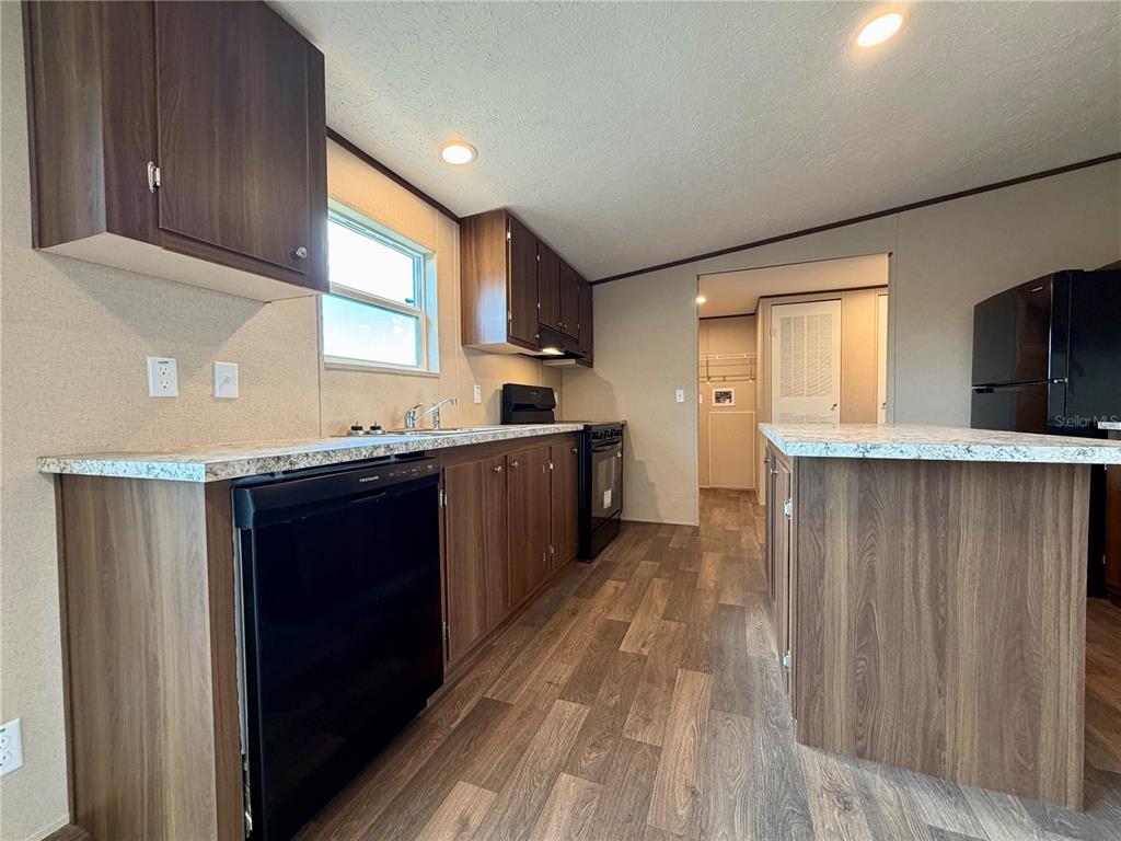 A kitchen features dark wood cabinets, speckled countertops, black appliances, and wood-look flooring — 4507 BIG TANK ROAD, LAKE WALES, FL