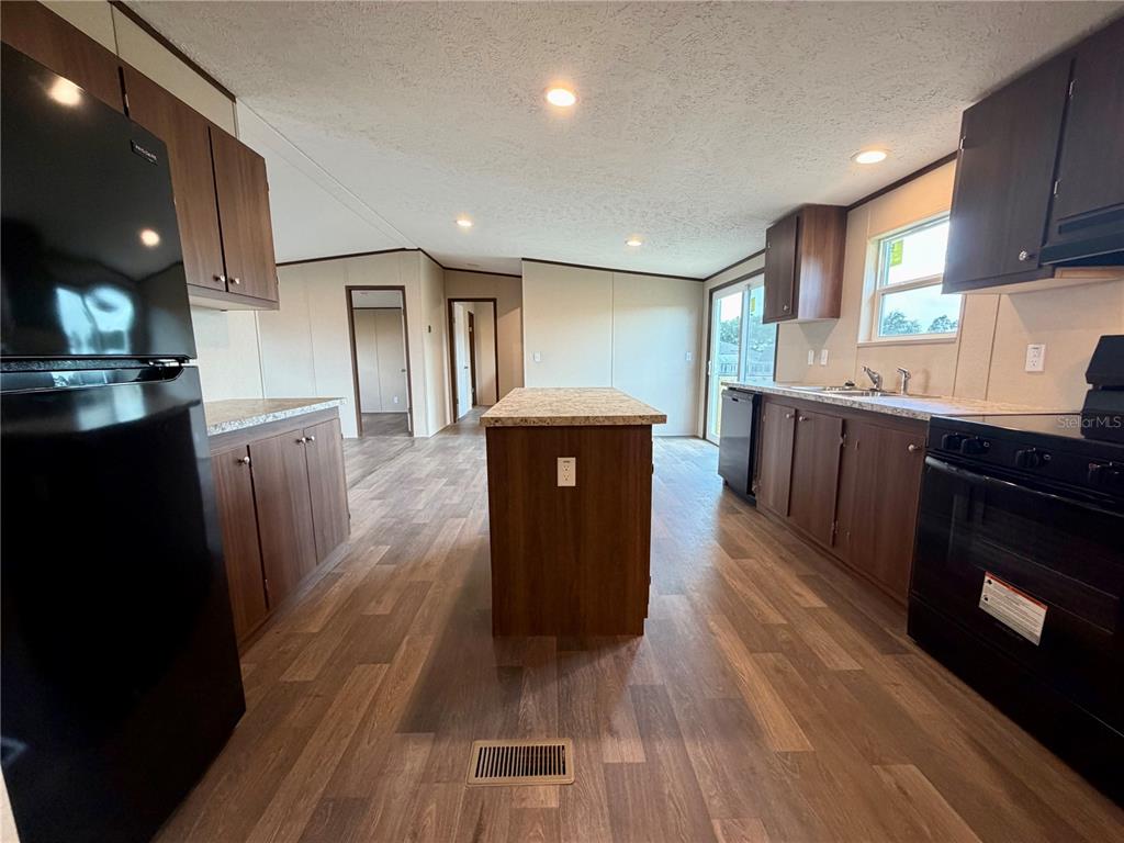 A kitchen features dark wood cabinets, a center island, and black appliances on wood flooring — 4507 BIG TANK ROAD, LAKE WALES, FL