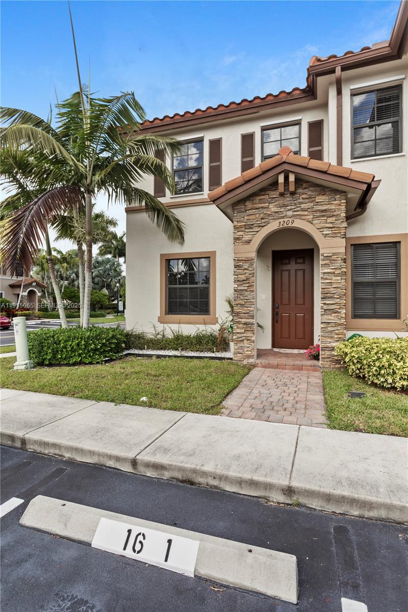 A two-story stucco townhouse features a stone-accented entryway and a paved walkway — 3209 SE 4th Ct, Homestead FL 33033, HOMESTEAD, FL