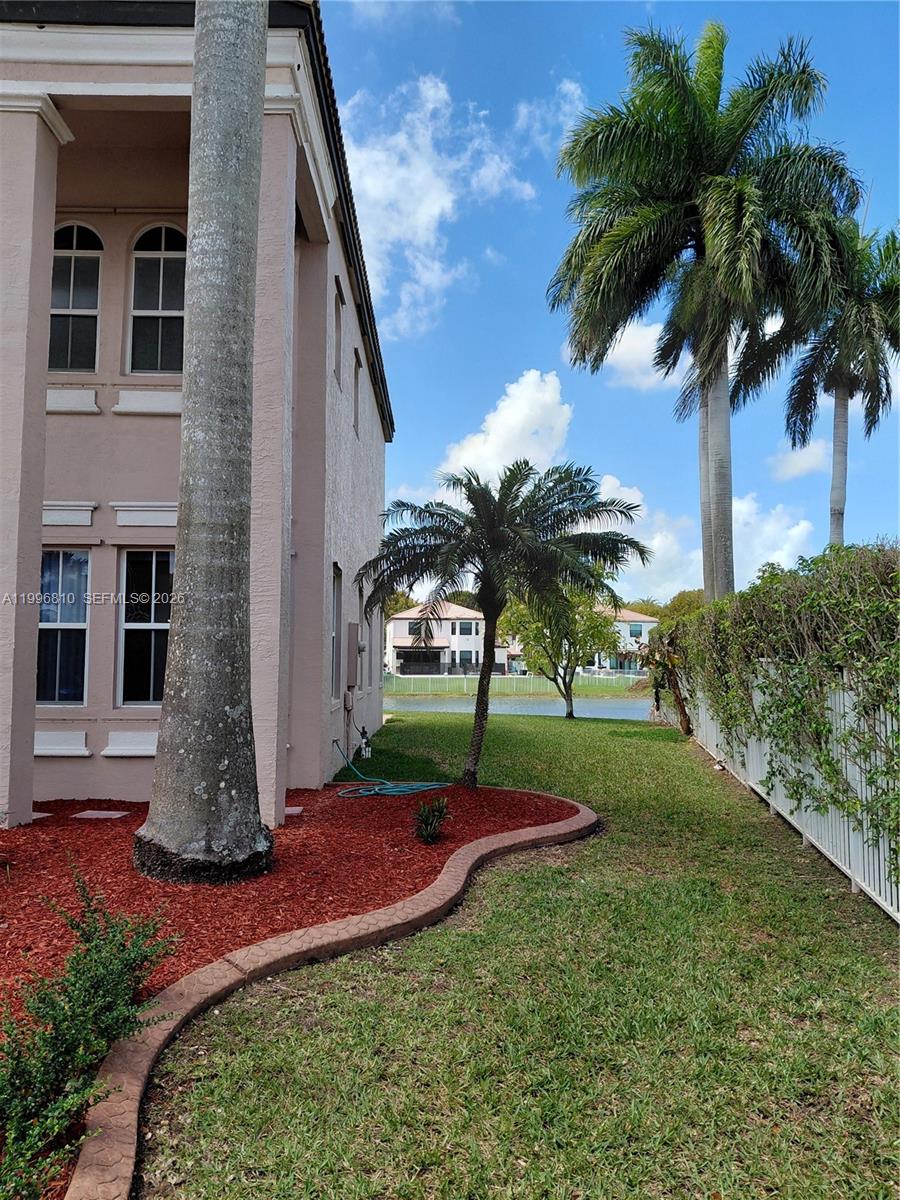 A side view of a house exterior features a lawn, palm trees, and a lake — 16863 SW 50th St, Miramar FL 33027, MIRAMAR, FL
