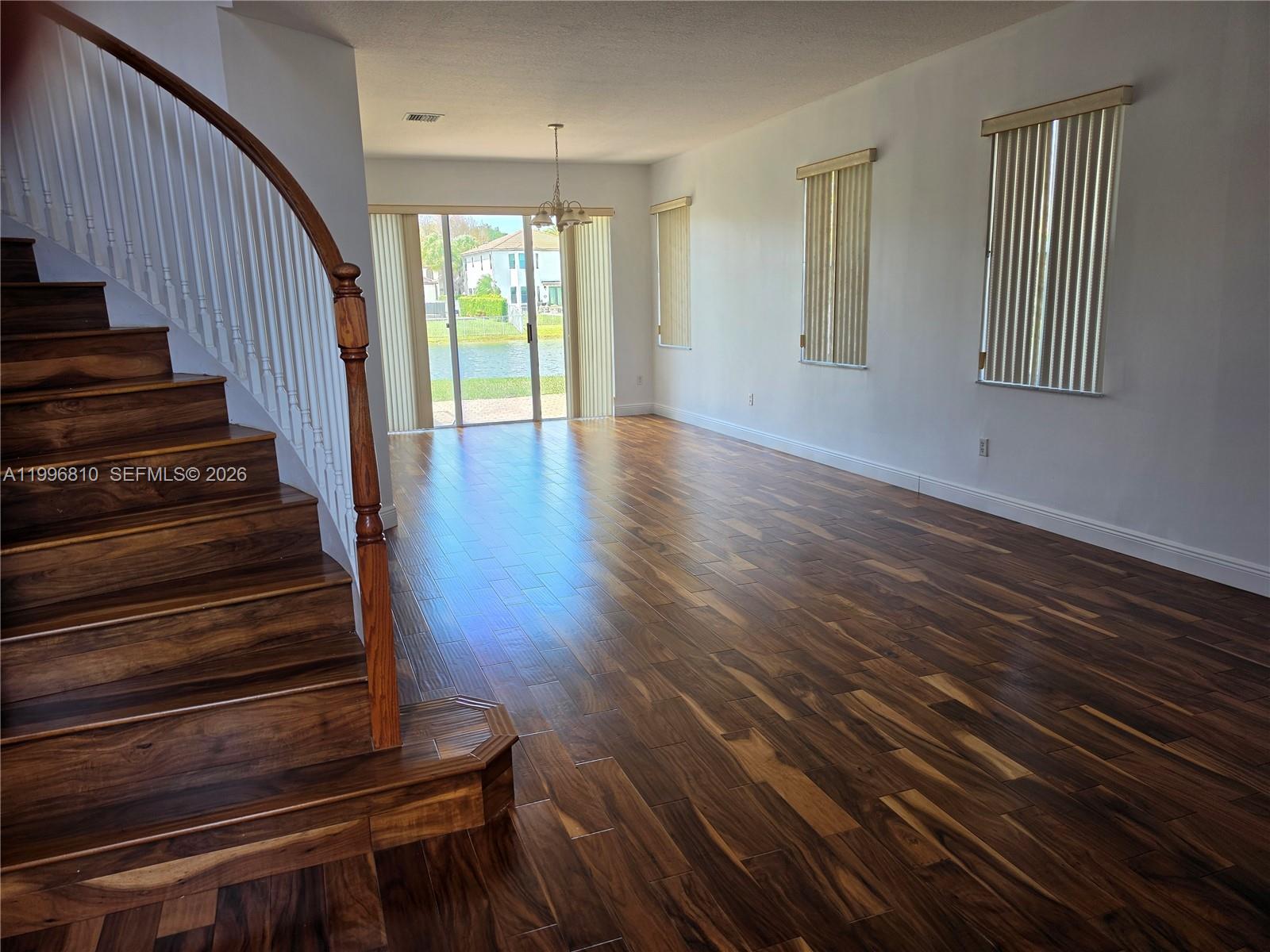 A living room features dark wood flooring, a curved staircase, and sliding glass doors — 16863 SW 50th St, Miramar FL 33027, MIRAMAR, FL