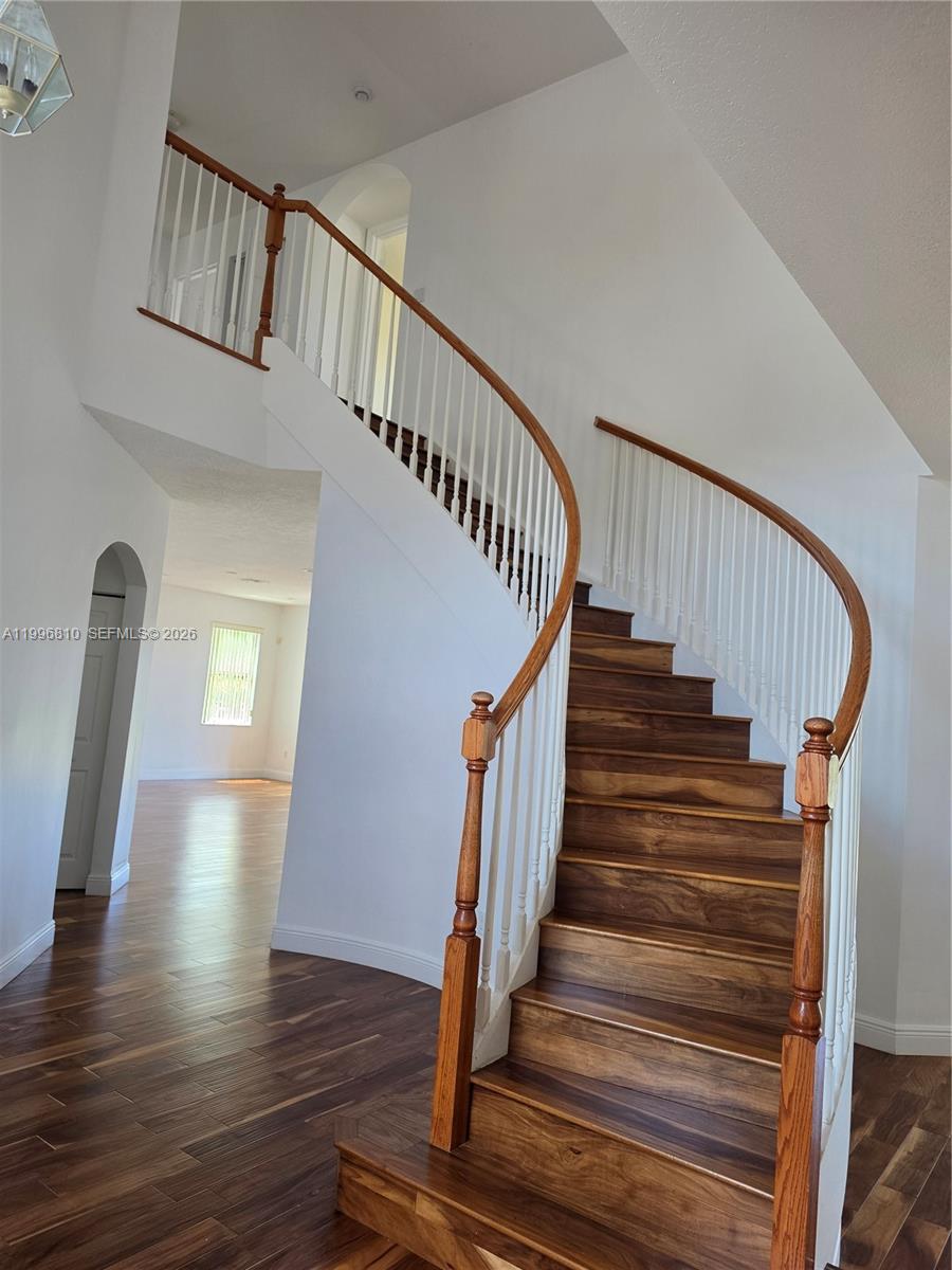 A curved wooden staircase with white balusters stands in a bright, open-concept home interior — 16863 SW 50th St, Miramar FL 33027, MIRAMAR, FL