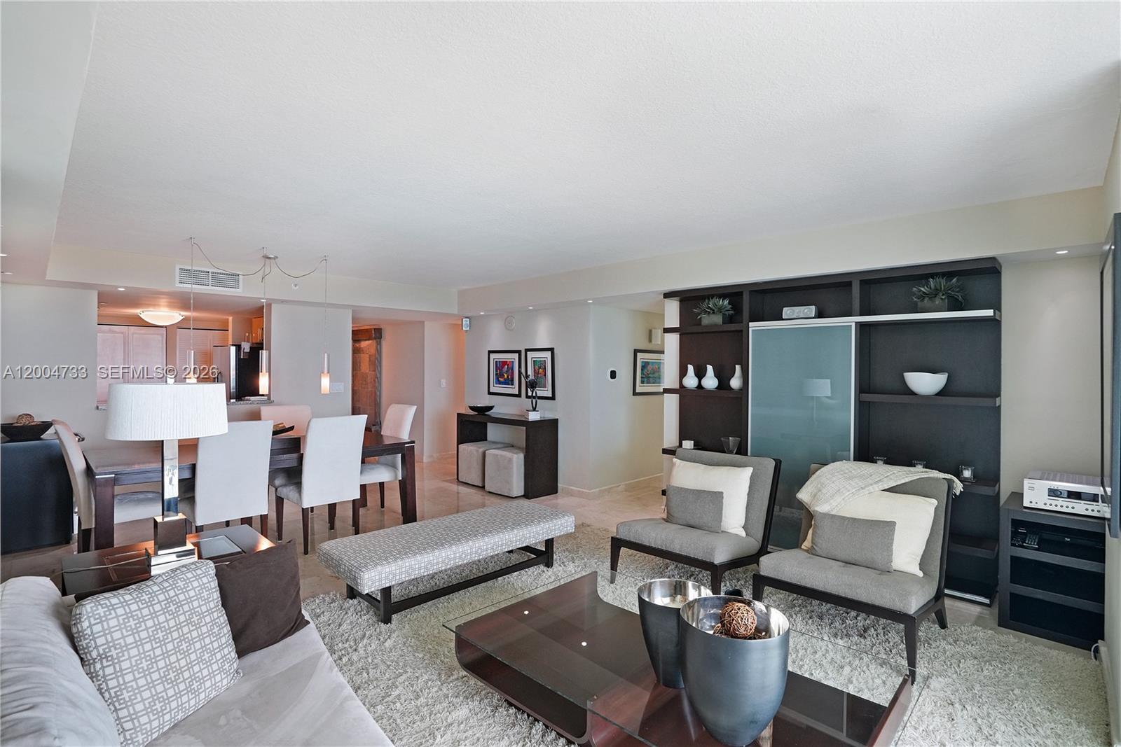 A modern living and dining area features neutral furniture, a glass coffee table, and shelving — 2101 Brickell Ave # 1812, Miami FL 33129, MIAMI, FL