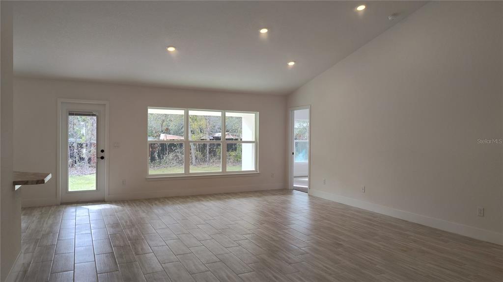 A bright living room features light wood-look tile flooring, recessed lighting, and large windows — 14159 GOLDFINCH ROAD, BROOKSVILLE, FL