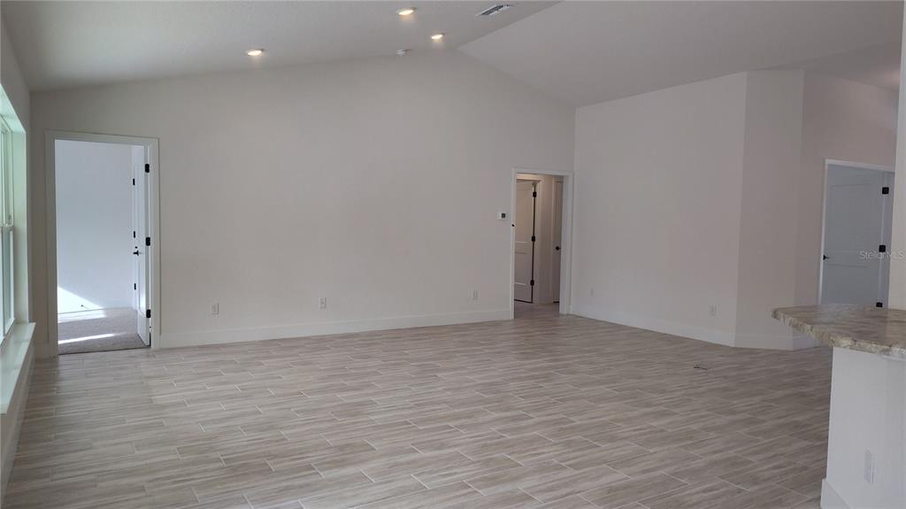 An empty room with vaulted ceilings, light tile flooring, and three doorways — 14159 GOLDFINCH ROAD, BROOKSVILLE, FL