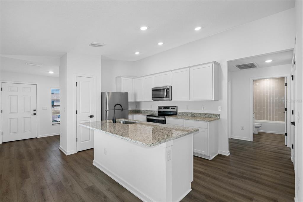 A kitchen with white cabinets, granite countertops, a center island, and wood-look flooring — 597 BLACKTHORN DRIVE, LAKELAND, FL
