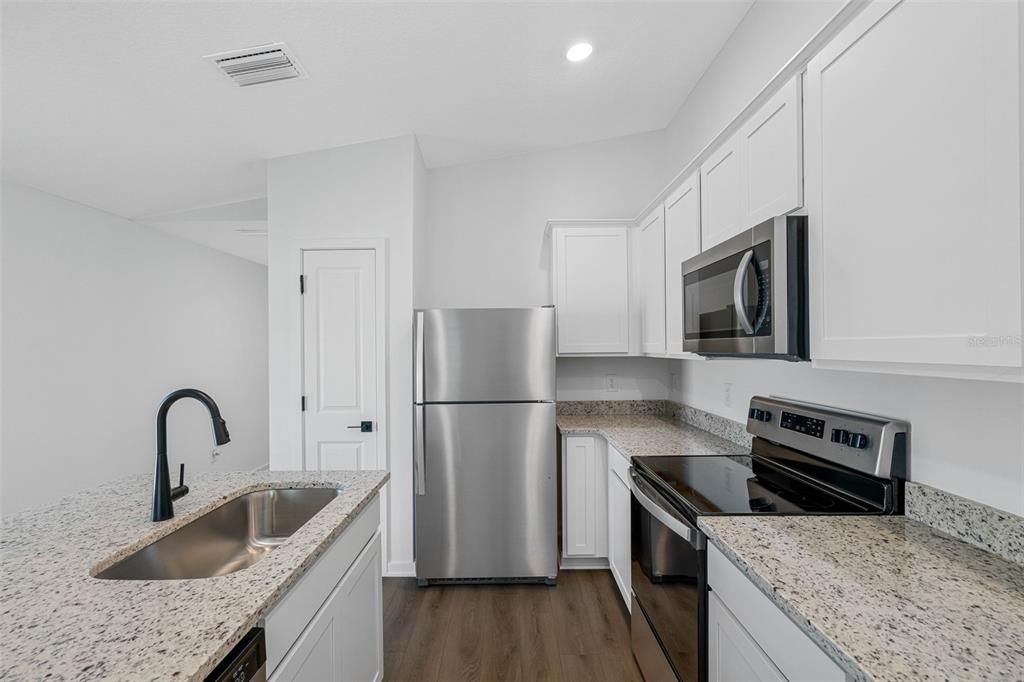 A kitchen features white cabinets, granite countertops, stainless steel appliances, and a dark faucet — 597 BLACKTHORN DRIVE, LAKELAND, FL