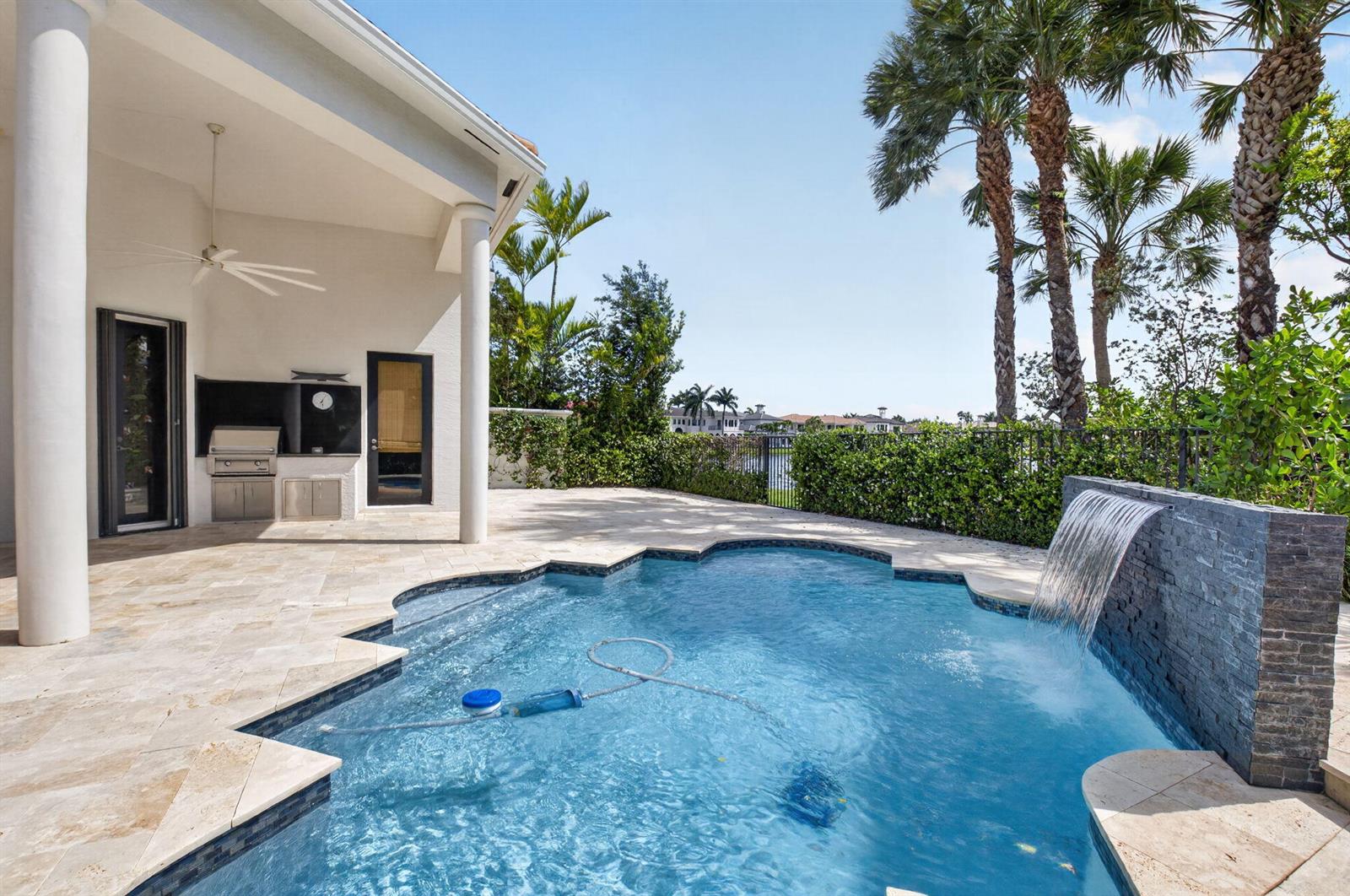 A patio with an outdoor kitchen and a swimming pool featuring a stone waterfall feature — 17921 Villa Club Way, Boca Raton FL 33496, BOCA RATON, FL