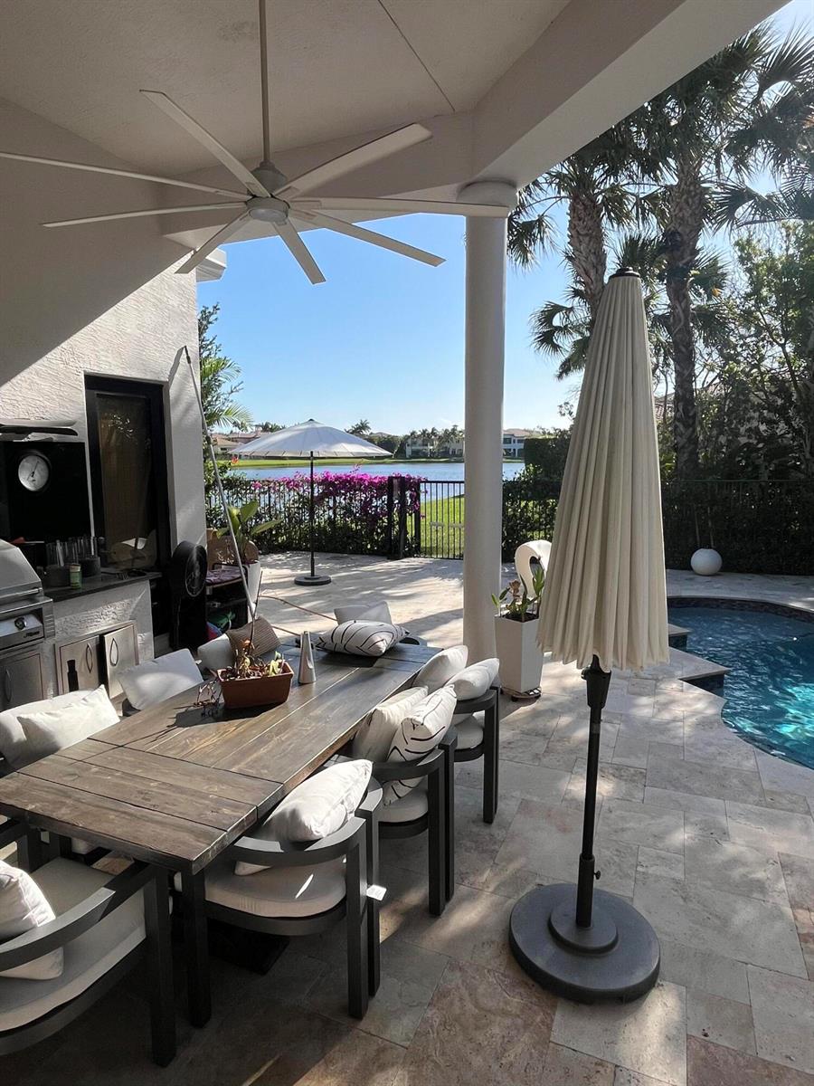 A covered patio features a wooden dining table, outdoor seating, and a pool by a lake — 17921 Villa Club Way, Boca Raton FL 33496, BOCA RATON, FL