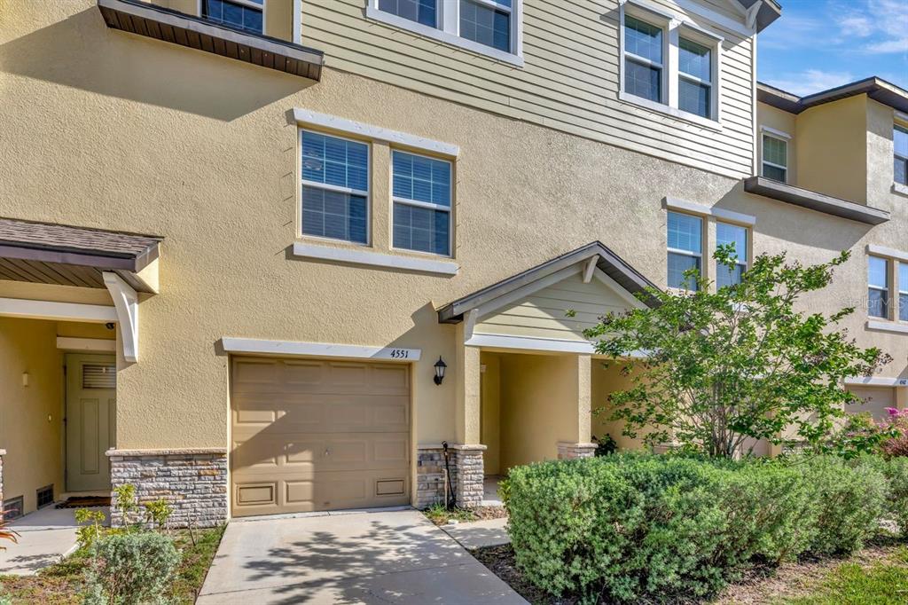 A two-story townhouse exterior features a single-car garage, beige stucco siding, and a small porch — 4551 TUSCAN LOON DRIVE, TAMPA, FL
