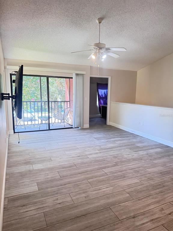 A living room features wood-look tile flooring, a ceiling fan, and a sliding glass balcony door — 5555 BAYWATER DRIVE, TAMPA, FL
