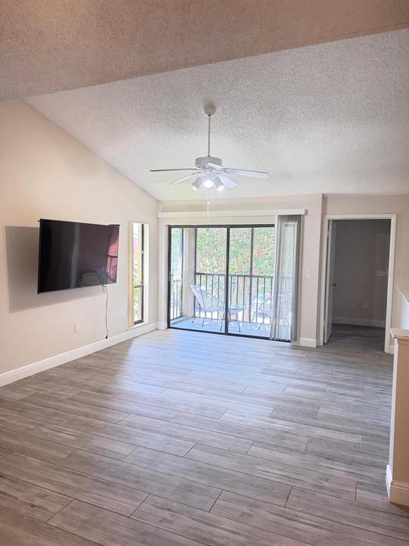 A living room features light wood-look tile flooring, a vaulted ceiling, and a sliding glass door — 5555 BAYWATER DRIVE, TAMPA, FL