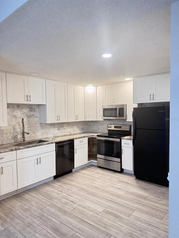 A kitchen features white cabinets, stainless steel appliances, a black refrigerator, and wood-look tile flooring — 5555 BAYWATER DRIVE, TAMPA, FL