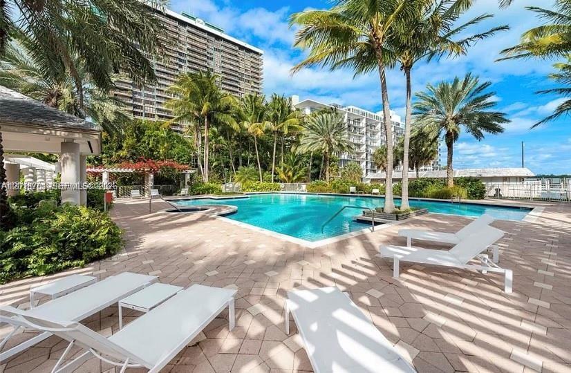 A swimming pool is surrounded by lounge chairs and palm trees near tall apartment buildings — 770 NE 69th St # 1E, Miami FL 33138, MIAMI, FL