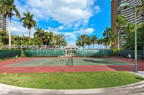 A tennis court surrounded by palm trees and a tall residential building under a blue sky — 770 NE 69th St # 1E, Miami FL 33138, MIAMI, FL