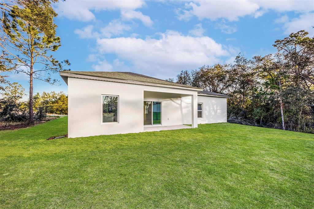 The exterior of a white stucco house features a covered patio and a grassy backyard — 381 AMBERJACK COURT, POINCIANA, FL