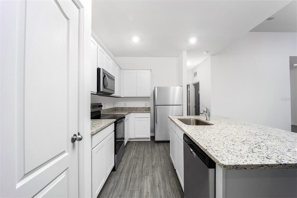 A kitchen features white cabinets, granite countertops, stainless steel appliances, and wood-look flooring — 381 AMBERJACK COURT, POINCIANA, FL