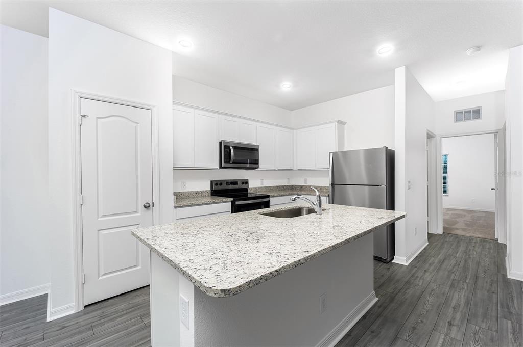 A kitchen features white cabinets, granite countertops, stainless steel appliances, and gray wood-look flooring — 381 AMBERJACK COURT, POINCIANA, FL