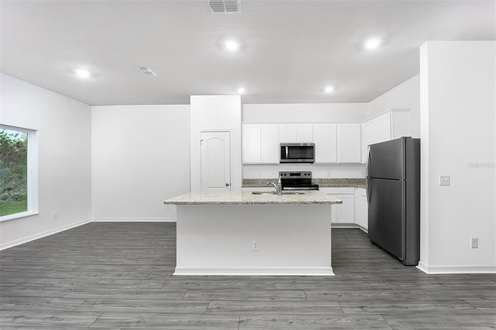 A kitchen features white cabinets, granite countertops, a center island, and gray wood-look flooring — 381 AMBERJACK COURT, POINCIANA, FL