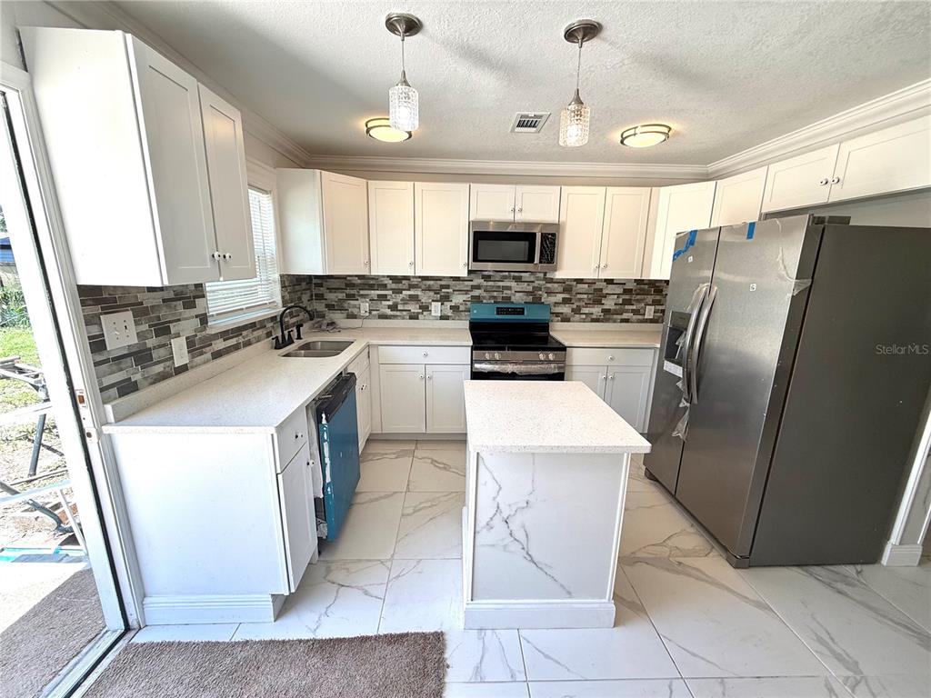 A kitchen features white cabinets, stainless steel appliances, a center island, and marble-look tile flooring — 1682 MAGNOLIA LANE, KISSIMMEE, FL