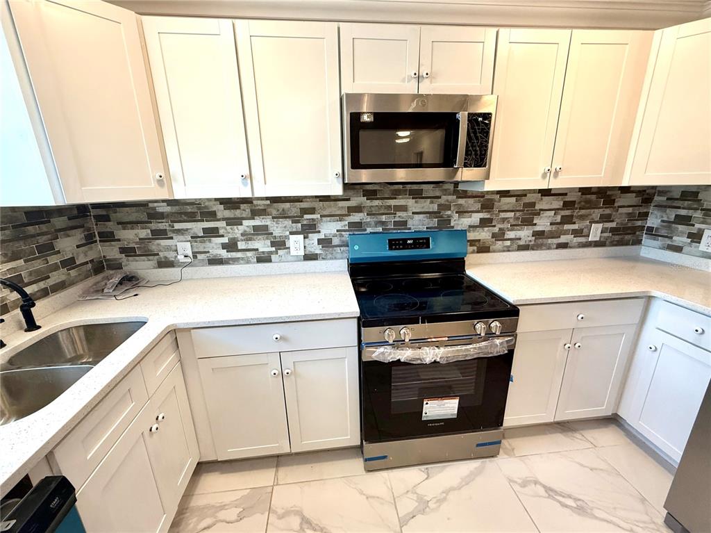 A kitchen features white cabinets, stainless steel appliances, a tiled backsplash, and light countertops — 1682 MAGNOLIA LANE, KISSIMMEE, FL
