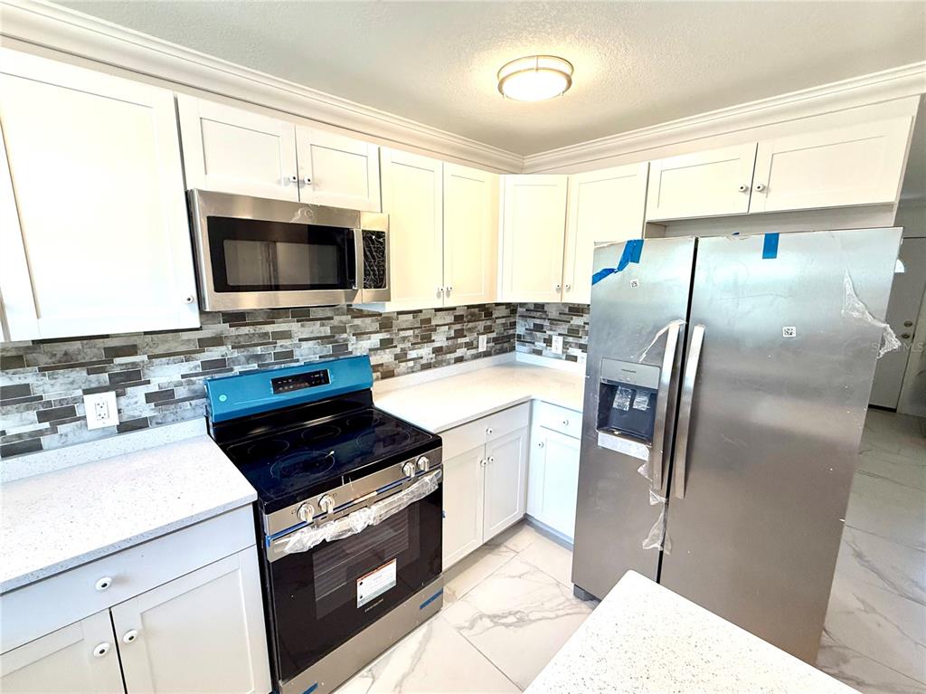 A kitchen features white cabinets, stainless steel appliances, a tiled backsplash, and light-colored countertops — 1682 MAGNOLIA LANE, KISSIMMEE, FL