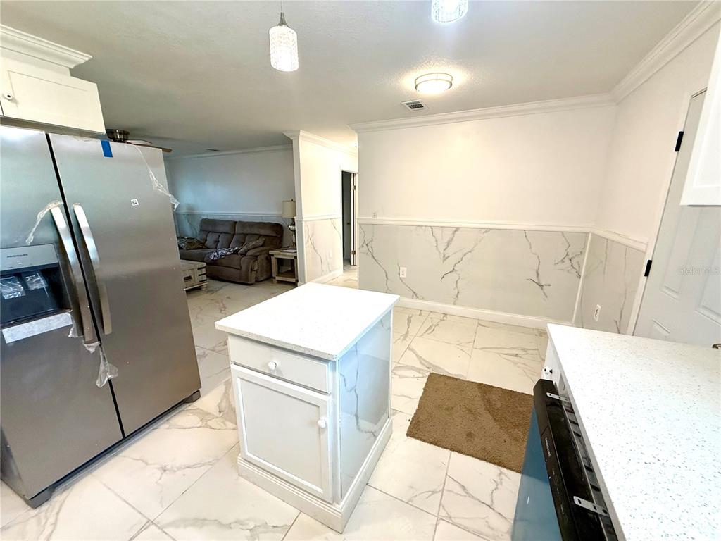 A kitchen features a central island, stainless steel refrigerator, and white marble-patterned tile flooring — 1682 MAGNOLIA LANE, KISSIMMEE, FL