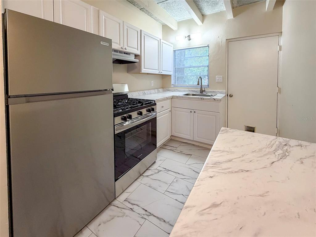 An empty room features wood-look flooring, exposed ceiling beams, and a ceiling fan — 219 NW 3RD AVENUE UNIT B, GAINESVILLE, FL