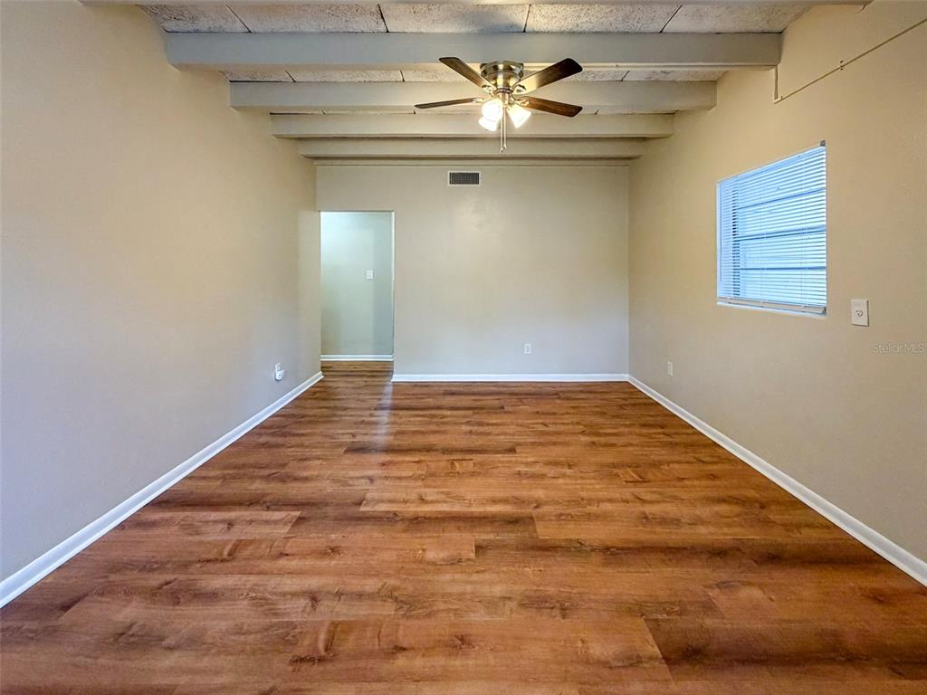 An empty room features wood-look flooring, a ceiling fan, and exposed ceiling beams — 219 NW 3RD AVENUE UNIT B, GAINESVILLE, FL