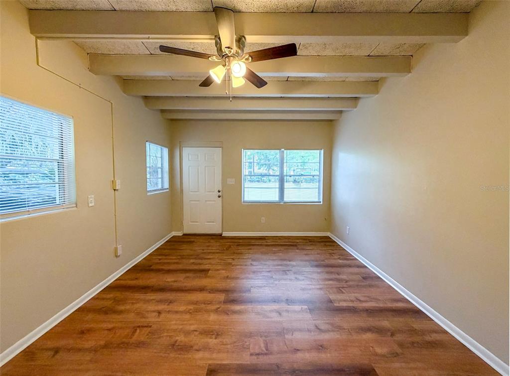 An empty room features wood-look flooring, exposed ceiling beams, a ceiling fan, and white walls — 219 NW 3RD AVENUE UNIT B, GAINESVILLE, FL