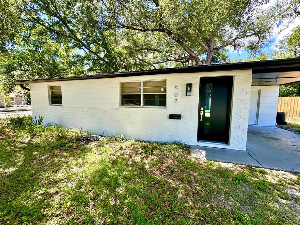 A black front door with a vertical glass panel sits beside a white brick wall — 502 E KNOLLWOOD STREET, TAMPA, FL