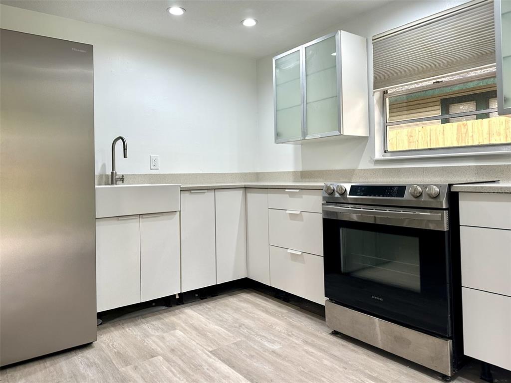 A modern kitchen features white flat-panel cabinetry, stainless steel appliances, and a farmhouse sink — 502 E KNOLLWOOD STREET, TAMPA, FL