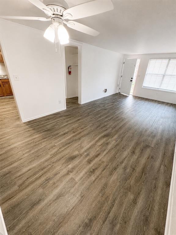 An empty living room features light wood-look flooring, white walls, and a ceiling fan — 420-420 MILLS STREET UNIT 32, LEESBURG, FL