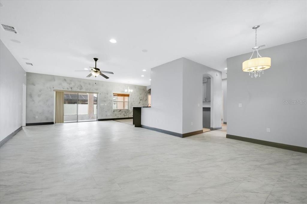 A spacious, open-concept living area features light-colored tile flooring, a ceiling fan, and a chandelier — 2850 SHELDON STREET, LAKELAND, FL