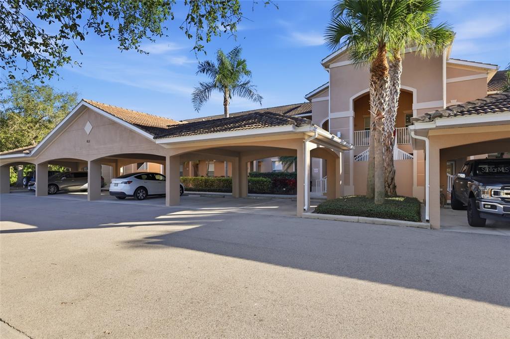 A covered parking area sits in front of a multi-story apartment building with palm trees — 803 FAIRWAYCOVE LANE UNIT 205, BRADENTON, FL