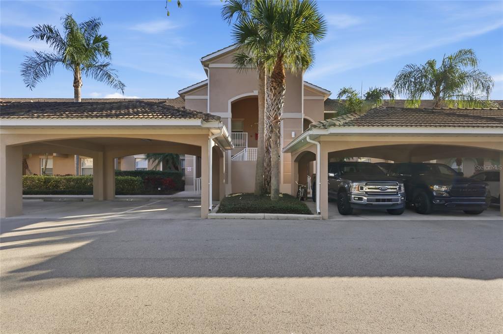 A beige apartment building exterior features two covered parking carports and palm trees — 803 FAIRWAYCOVE LANE UNIT 205, BRADENTON, FL