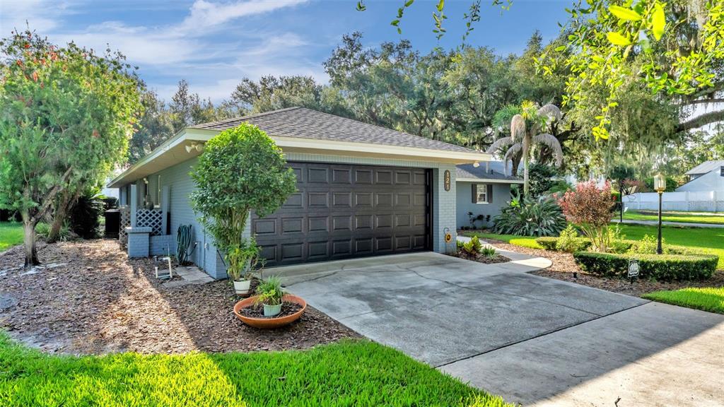 A gray house with a dark garage door and a concrete driveway sits on a lawn — 121 SHADOW LANE, LAKELAND, FL