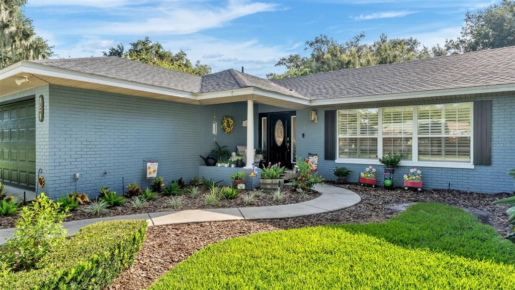 A blue brick house features a dark front door, a walkway, and a landscaped yard — 121 SHADOW LANE, LAKELAND, FL