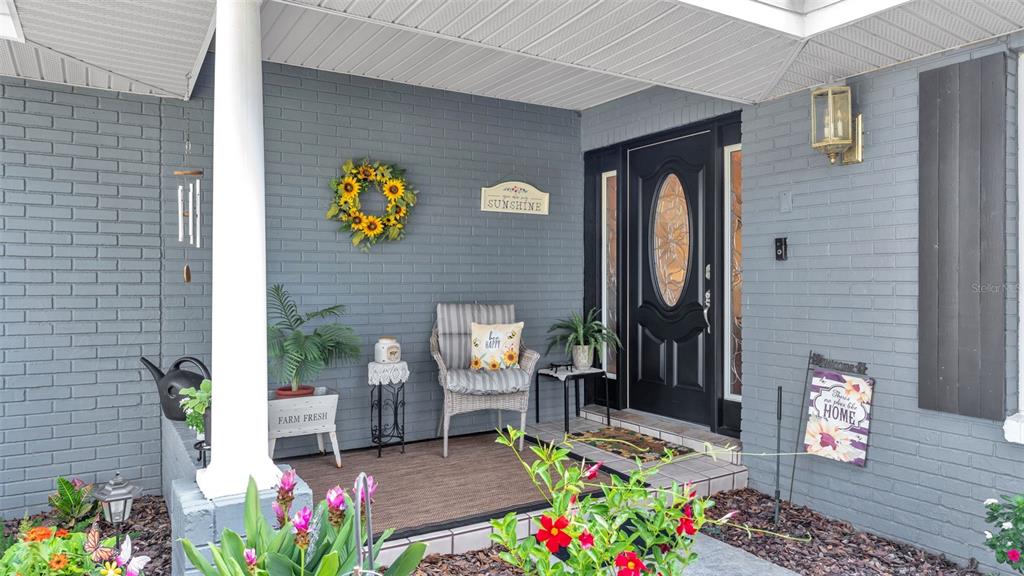 A gray brick porch features a black front door, a wicker chair, and potted plants — 121 SHADOW LANE, LAKELAND, FL