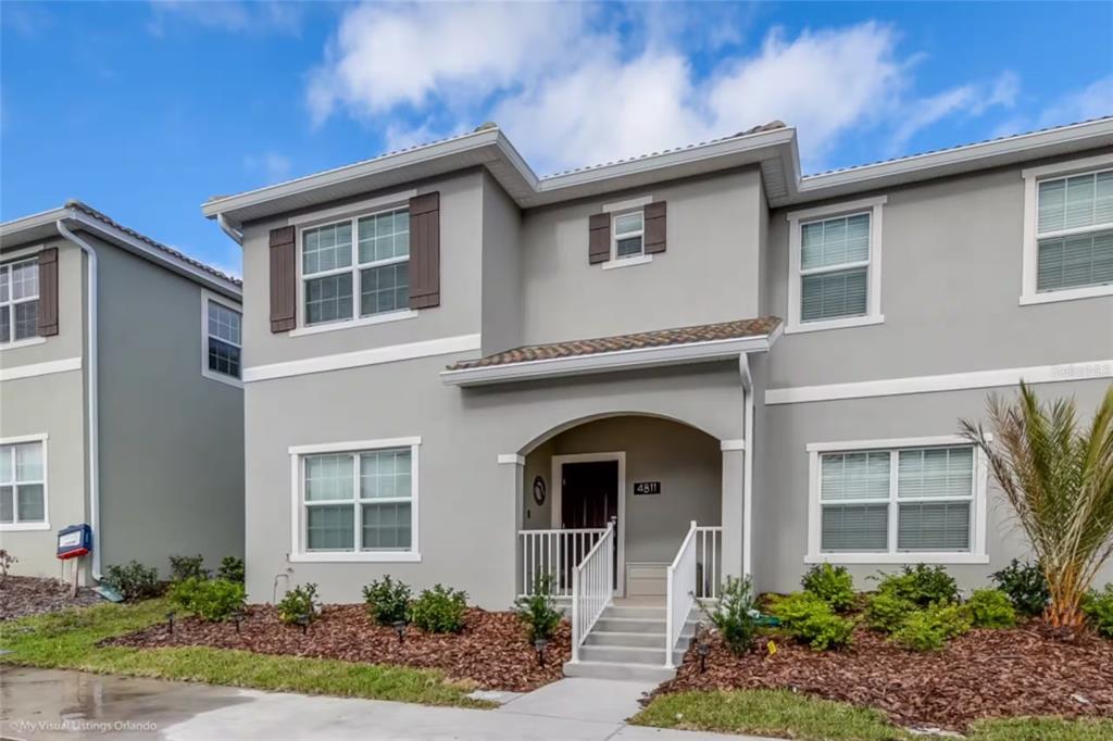 A two-story gray stucco townhouse with a covered front porch and white railings — 4811 LULLABY LANE, KISSIMMEE, FL