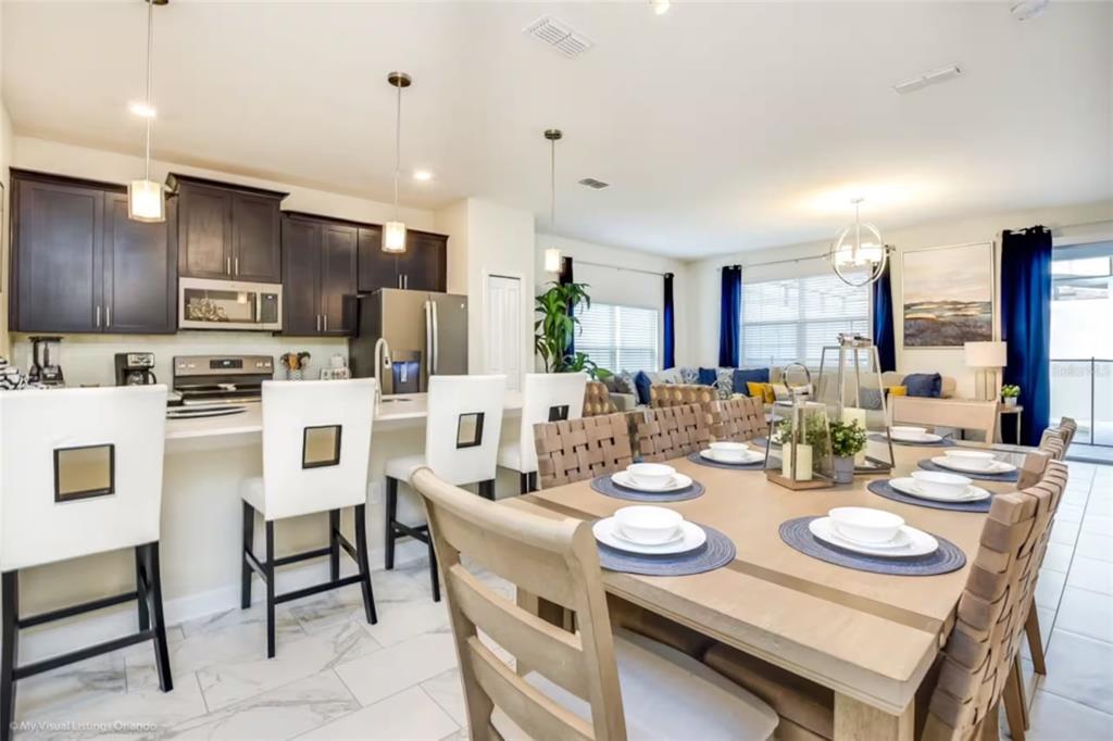 An open-concept kitchen and dining area featuring dark cabinetry, white countertops, and a wooden table — 4811 LULLABY LANE, KISSIMMEE, FL