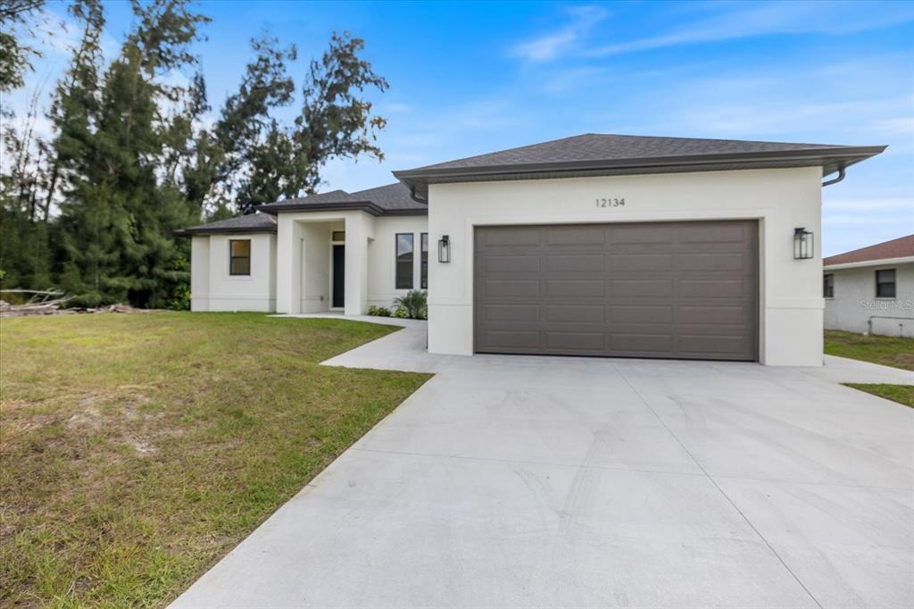 A modern, single-story house features a white stucco exterior, a brown garage door, and a driveway — 12134 MALLORCA AVENUE, NORTH PORT, FL