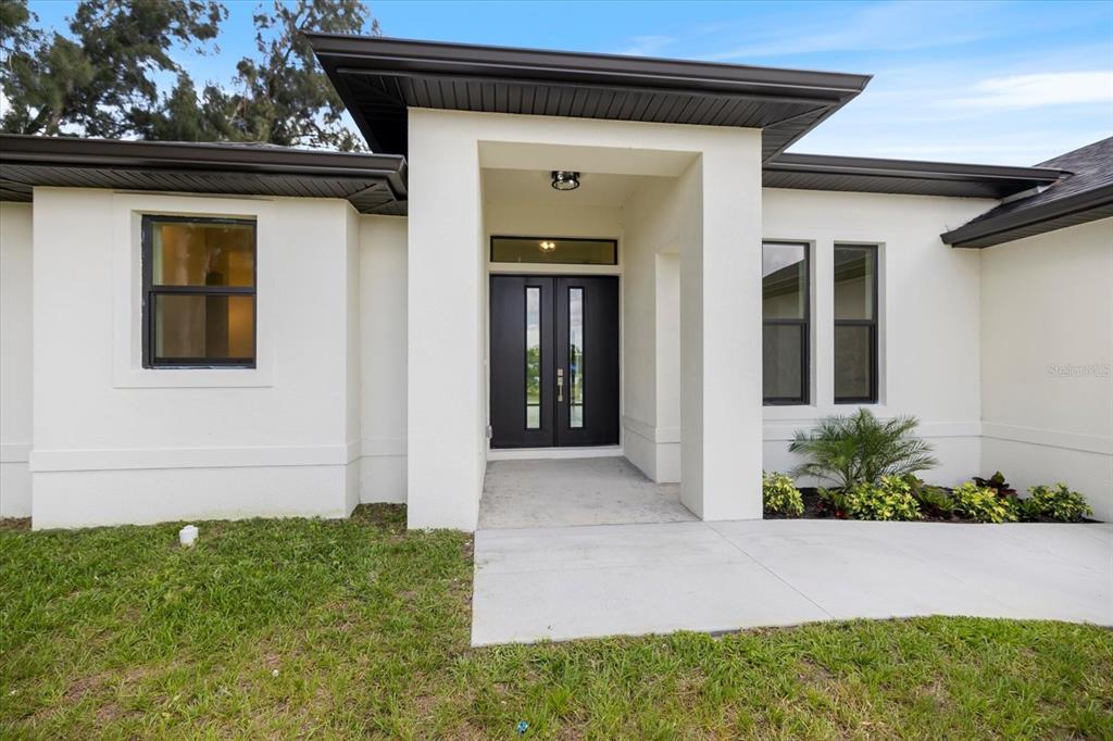 The exterior of a modern white house features a dark double front door and windows — 12134 MALLORCA AVENUE, NORTH PORT, FL