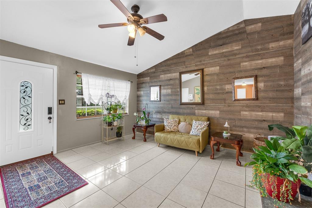 A living room features a vaulted ceiling, tile floors, and a wood-plank accent wall — 8509 LYONIA DRIVE, ORLANDO, FL