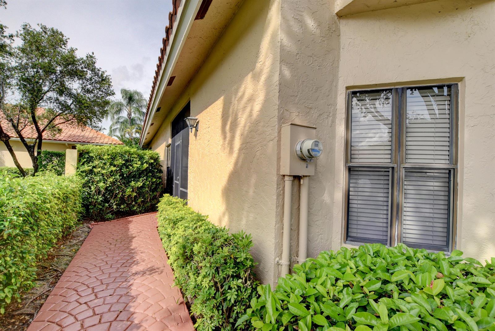 A paved walkway leads along the side of a beige house with a utility meter — 22667 Meridiana Drive, Boca Raton FL 33433, BOCA RATON, FL