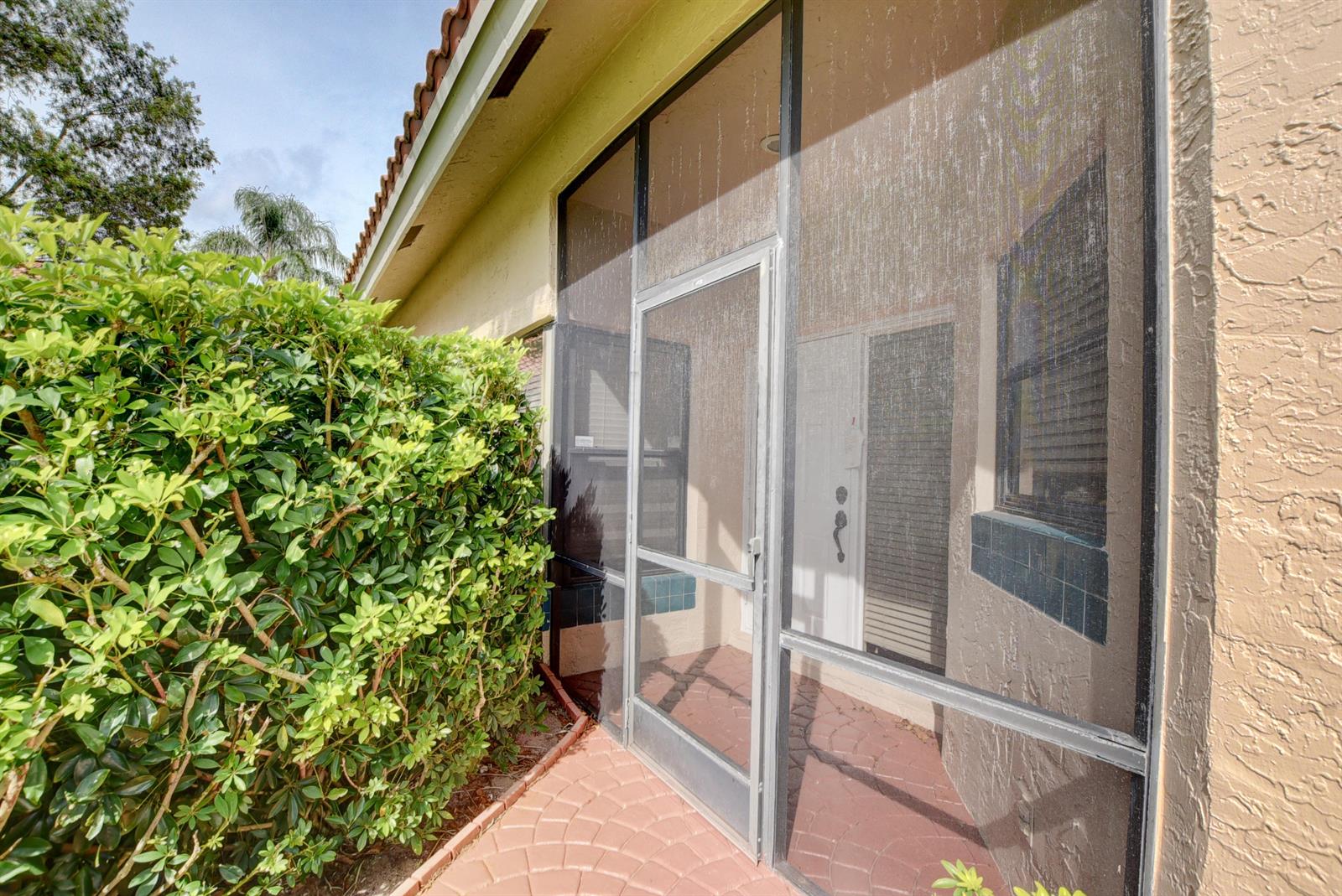 A screened-in entryway features a metal door, tiled flooring, and an adjacent green hedge — 22667 Meridiana Drive, Boca Raton FL 33433, BOCA RATON, FL