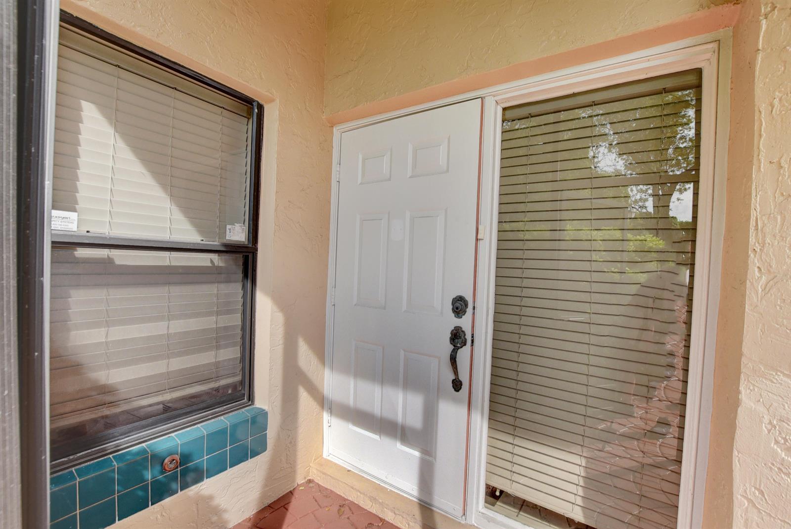 A white front door with a side window and a tiled ledge sits outdoors — 22667 Meridiana Drive, Boca Raton FL 33433, BOCA RATON, FL