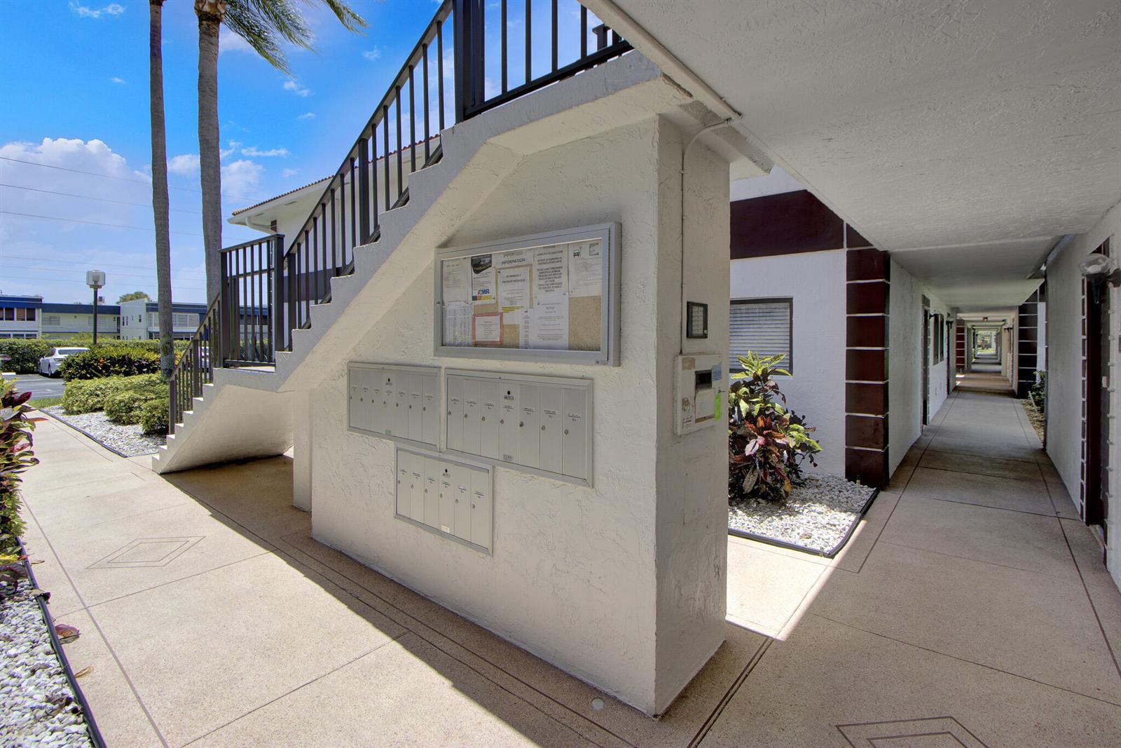 An outdoor apartment complex walkway features a staircase, mailboxes, and a bulletin board — 15451 Pembridge Drive # 206, Delray Beach FL 33484, DELRAY BEACH, FL