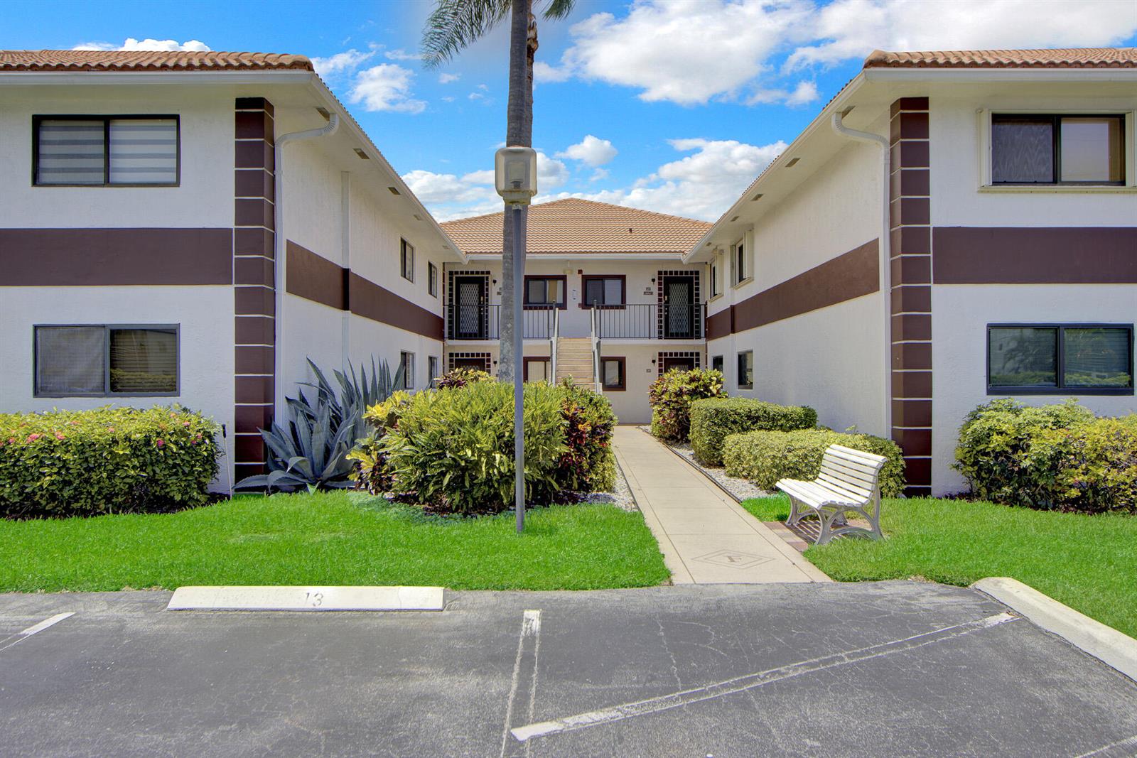 A two-story apartment building exterior features a central walkway, landscaping, and a parking lot — 15451 Pembridge Drive # 206, Delray Beach FL 33484, DELRAY BEACH, FL