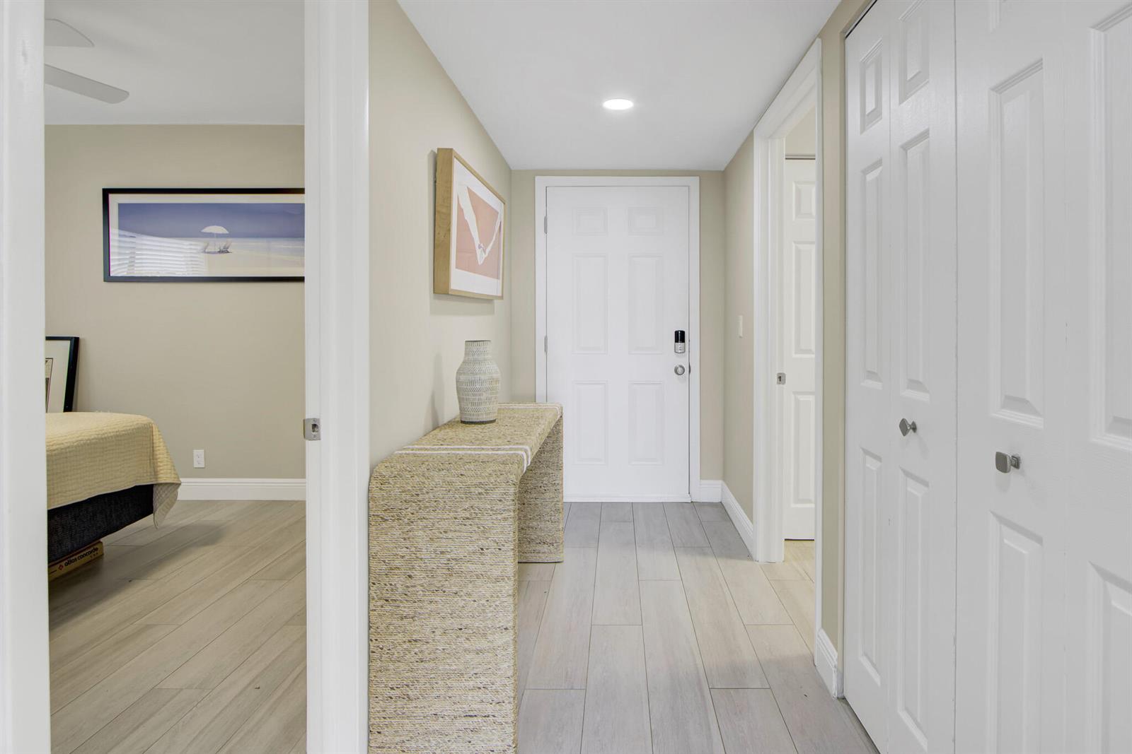 A hallway with light wood-look tile flooring leads to a white front door — 15451 Pembridge Drive # 206, Delray Beach FL 33484, DELRAY BEACH, FL